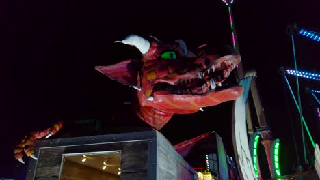 Gorgeous-shot-of-a-revolving-head-of-an-automated-dragon-over-the-entrance-of-a-ride-in-an-amusement-park-in-London,-UK-at-night-time