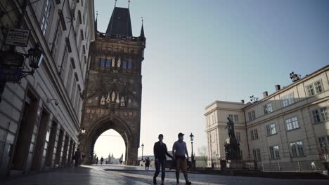 Couple-or-pair-walking-under-Old-Town-Bridge-Tower-Gate-in-Prague,-low-wide-angle-view,-Czech-Republic