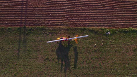 Above-stationary-yellow-Gyrocopter-with-white-blade-in-rural-field,-top-down