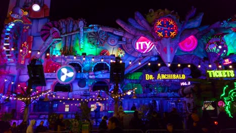 Pan-shot-of-colorful-amusement-park-ride-inside-amusement-park-at-night-time-in-London,-UK-with-locals-walking-around