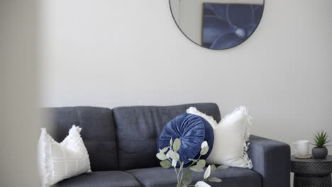 Modern-contemporary-styled-home-dark-couch-navy-blue-and-white-cushions-circle-mirror-coffee-table-with-vase-and-stem