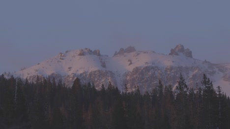 Rosafarbenes-Sonnenuntergangslicht-Auf-Hohen-Berggipfeln-Mit-Wind,-Der-Die-Bäume-Im-Vordergrund-Weht