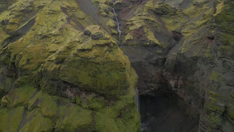 Waterfall-drone-shot-as-water-drops-aggressively-over-a-rocky-greenish-yellow-ledge-into-a-plunge-pool-below