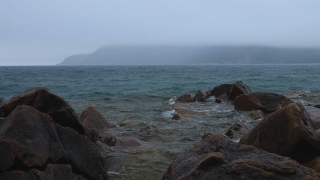 Handheld-shot-of-small-waves-lapping-the-rocky-shoreline-of-Lake-Superior-in-the-rain