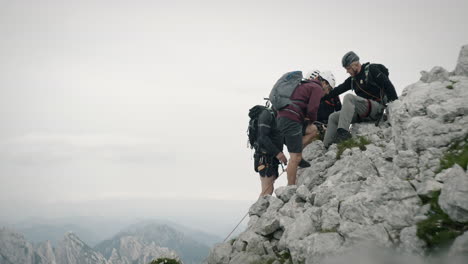 Un-Grupo-De-Excursionistas-Se-Detiene-Para-Descansar-En-La-Roca-En-Las-Montañas,-Usando-Un-Equipo-De-Escalada-Completo