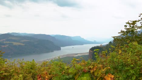 HD-Boom-up-with-autumn-colored-hedges-in-foreground-and-the-Vista-House-on-a-cliff-in-the-distance-overlooking-the-Columbia-River-with-mostly-cloudy-sky-take-four