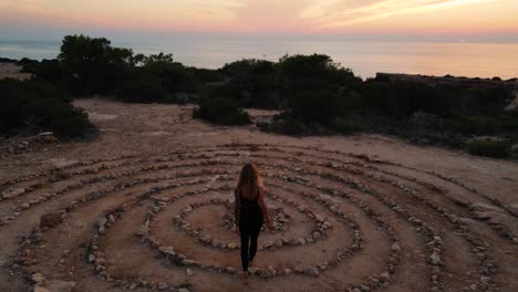 Drone-view-of-woman-on-time-space-on-ground-spiral-coiled-stones-with-sunset-sky