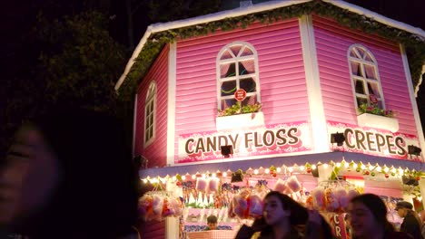 Low-angle-shot-of-cotton-candy-and-crepes-available-in-a-pink-stall-inside-an-amusement-park-in-London,-UK-at-night-time