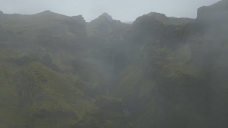 Volando-A-Través-De-Las-Nubes-Para-Revelar-Una-Majestuosa-Cascada,-Cañón,-Río-Y-Valle-Verde