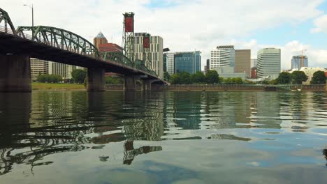 4K-Nice-low-on-the-water-shot-with-slight-pan-left-to-right-of-Hawthorne-Bridge-crossing-Willamette-River-toward-downtown-Portland,-Oregon-skyline-with-mostly-cloudy-sky