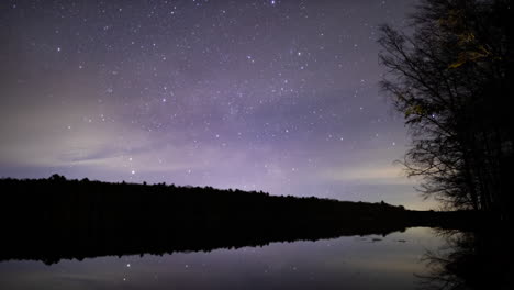 A-time-lapse-of-a-thin-layer-of-clouds-moving-over-a-small-lake,-obscuring-the-stars-as-they-move-through-the-sky
