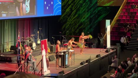 Indigenous-people-performing-ceremonial-welcome-dance,-spiritual-cleansing-at-the-supersized-grand-Australian-citizenship-ceremony-at-great-hall-of-Brisbane-convention-and-exhibition-centre