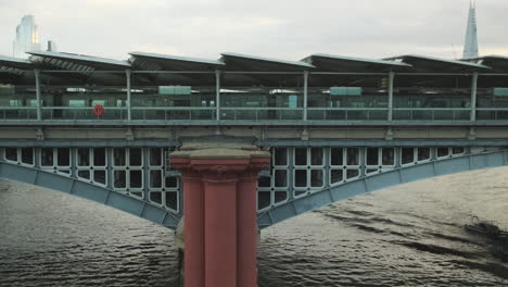 London-Blackfriars-Station-Bridge,-Tugboat-on-River-Thames-Passing-Underneath-and-Old-Red-Pillars-in-Foreground