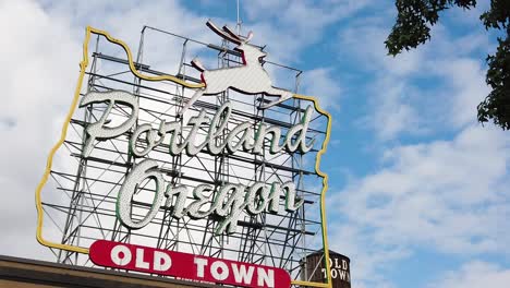 HD-Static-Portland-Oregon-Old-Town-sign-in-left-center-frame-with-Old-Town-water-tower-peeking-through-and-out-from-sign-with-partly-cloudy-sky