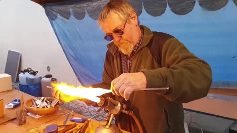 Glassblower-artisan-shaping-the-hot-molten-glass-at-strong-fire-inside-a-workshop
