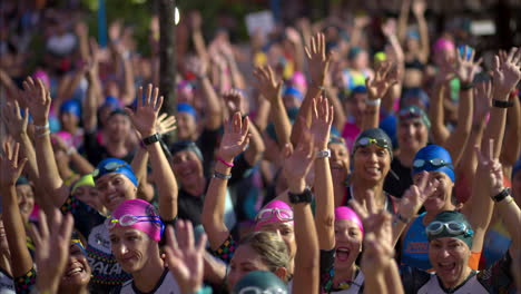 Large-group-of-female-athletes-with-colorful-caps-cheering-with-their-arms-up-before-the-triathlon-starts