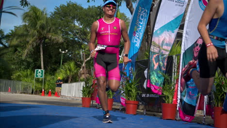 Two-young-male-athletes-wearing-a-pink-and-a-blue-suit-and-sunglasses-sprinting-to-the-finish-line-of-a-triathlon-competition