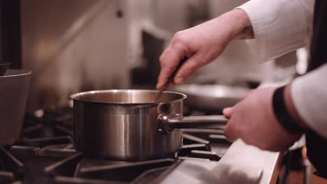 Cook-scoops-through-a-saucepan-with-a-spatula-while-steam-comes-from-a-frying-pan-in-the-background