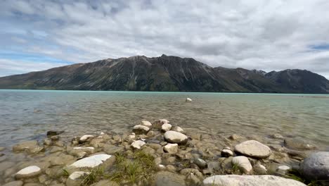 Low-angle-view-from-shore-of-turquoise-glacier-lake-and-rugged-mountain-face