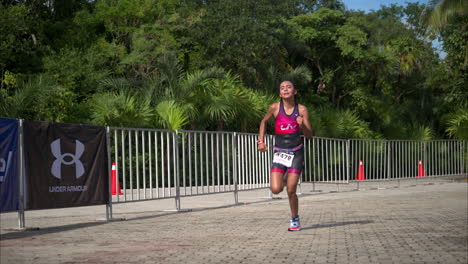 Slow-motion-of-a-teenage-athlete-wearing-a-pink-and-purple-suit-running-the-final-stage-of-a-triathlon-competition