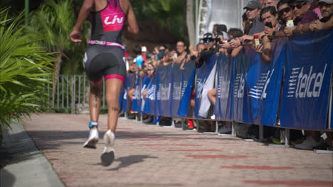 Latin-female-athlete-running-passing-by-a-crowd-of-spectators-cheering-the-participants-at-a-triathlon-competition