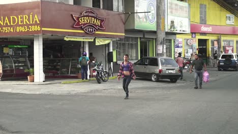 Trans-male-walking-on-the-road-in-front-of-Servipan-traditional-bakery,-Slow-motion-advancing-shot