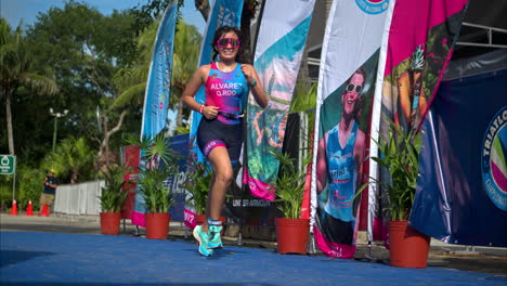 Slow-motion-of-a-young-female-athlete-in-a-suit-running-to-the-finish-line-of-a-triathlon-competition-looking-exhausted