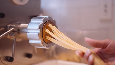 Male-cook-accompany-the-long-strands-of-spaghetti-from-the-pasta-machine