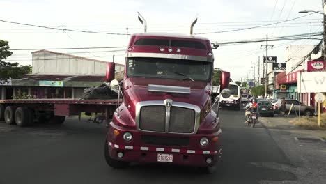 Camión-Semirremolque-Rojo-Con-Cama-De-Carga-Vacía-Girando-A-La-Derecha-En-Una-Concurrida-Avenida,-Cámara-Lenta-De-Tiro-Medio