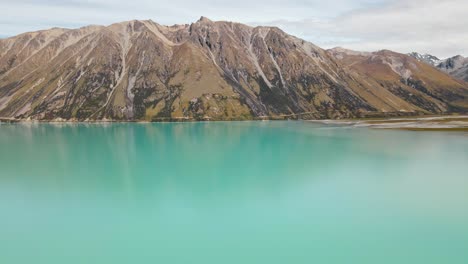 Aerial-footage-of-majestic-mountain-reflecting-in-turquoise-lake-water-in-New-Zealand