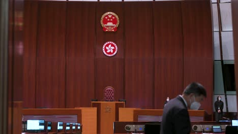 Gesetzgeber-Erreichen-Die-Hauptkammer-Des-Legislativrates,-Während-Die-Embleme-Der-Volksrepublik-China-Im-Hintergrund-Zu-Sehen-Sind