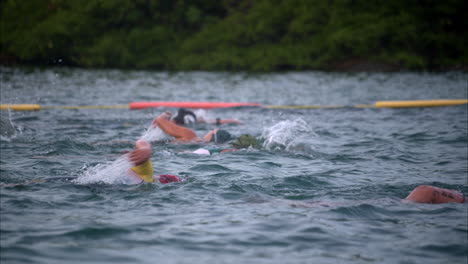 Grupo-De-Atletas-Nadando-Con-Aspecto-Cansado-Agotado-En-Una-Competición-De-Triatlón-Con-Gorras-Y-Gafas