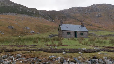 A-slow-left-panning-shot-reveals-a-old-stone-building-against-a-mountain-backdrop-in-the-Highlands-of-Scotland-along-the-shores-of-Loch-Gleann-Dubh