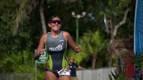 Slow-motion-of-a-teenage-female-athlete-finishing-a-triathlon-competition-running-celebrating-with-her-arms-up