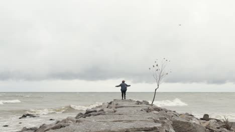 Lonely-woman-standing-pensively-at-the-end-of-a-stone-breakwater-on-a-stormy-day