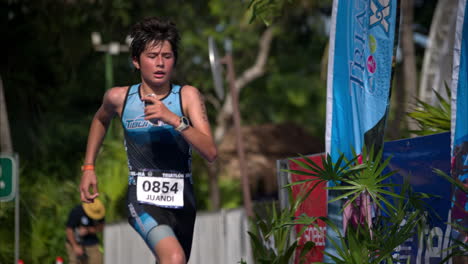 Slow-motion-of-a-teenage-young-male-athlete-in-a-blue-suit-finishing-a-triathlon-competition-looking-tired-and-exhausted