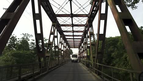 Public-transport-bus-crossing-single-lane-rusty-bridge,-Slow-motion-forward-shot