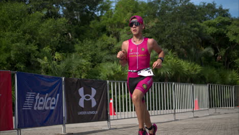 Slow-motion-of-a-young-athlete-wearing-a-pink-suit-and-sunglasses-running-at-a-triathlon-competition-passing-by