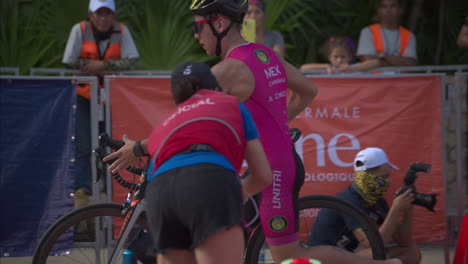 Latin-teenage-boy-competitor-getting-off-his-bike-barefooted-while-entering-the-transition-zone-at-a-triathlon-competition-wearing-a-pink-suit