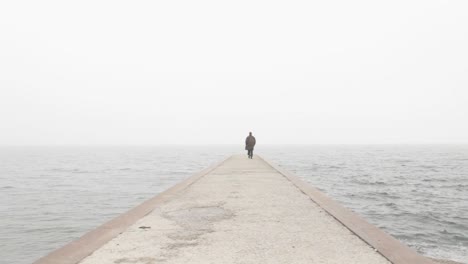 Person-walking-on-the-concrete-pier-on-a-foggy-day-at-sea
