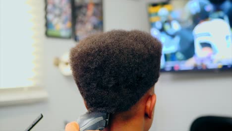 Black-boy-getting-a-Haircut-in-slow-motion-by-Barber-with-cordless-clippers,-close-up-static-view