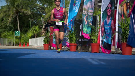 Slow-motion-of-a-male-young-athlete-in-a-pink-suit-jogging-entering-the-finish-line-of-a-triathlon-competition