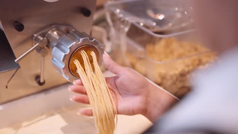 Male-cook-accompany-the-long-strands-of-spaghetti-from-the-pasta-machine