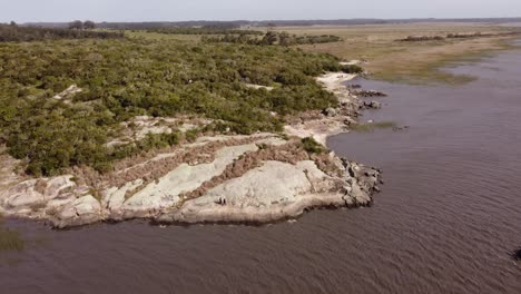 Luftbahnaufnahme-Eines-Paares,-Das-über-Felsen-An-Der-Schwarzen-Lagune-In-Punta-Del-Diablo,-Uruguay,-Geht