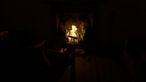An-old-chair-is-illuminated-in-a-dark-room-by-the-flickering-light-from-a-log-fire-in-an-old-fireplace