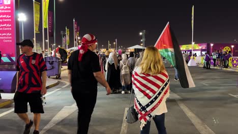 A-Girl-riding-skate-board-or-scooter-with-hijab-and-couple-are-walking-to-enter-Qatar-stadium-football-games-with-USA-scarf-or-flag-fashion-designed-for-watching-the-challenging-exciting-game-together