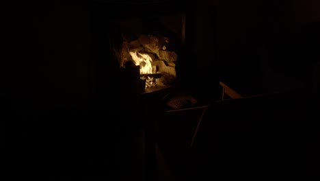 An-old-chair-is-illuminated-in-a-dark-room-by-the-light-from-a-log-fire-in-an-old-fireplace