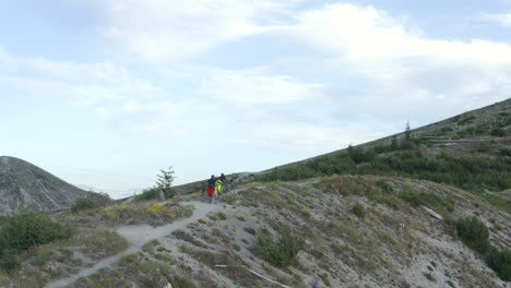 Two-friends-with-mountainbikes-walking-uphill-on-mountain-ridge-trail,-Mount-St