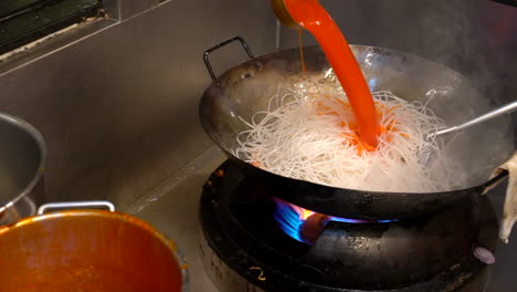 Thailand,-Bangkok---18-August-2022:-Preparing-pad-thai-adding-sauce-and-hot-water-to-rice-noodles-into-a-hot-wok-pan-in-restaurant