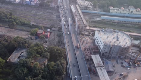 Aerial-shot-slowly-revealing-vehicles-crossing-through-Majerhat-over-bridge-road-alongside-new-construction-site-of-metro-line-and-railway-station-surrounded-by-cityscape